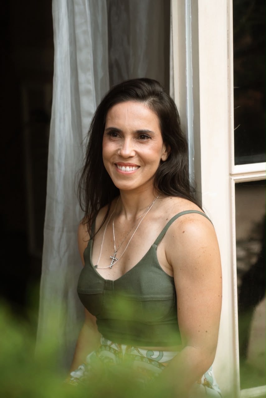 Érica Duque sorrindo, apoiada na janela de casa