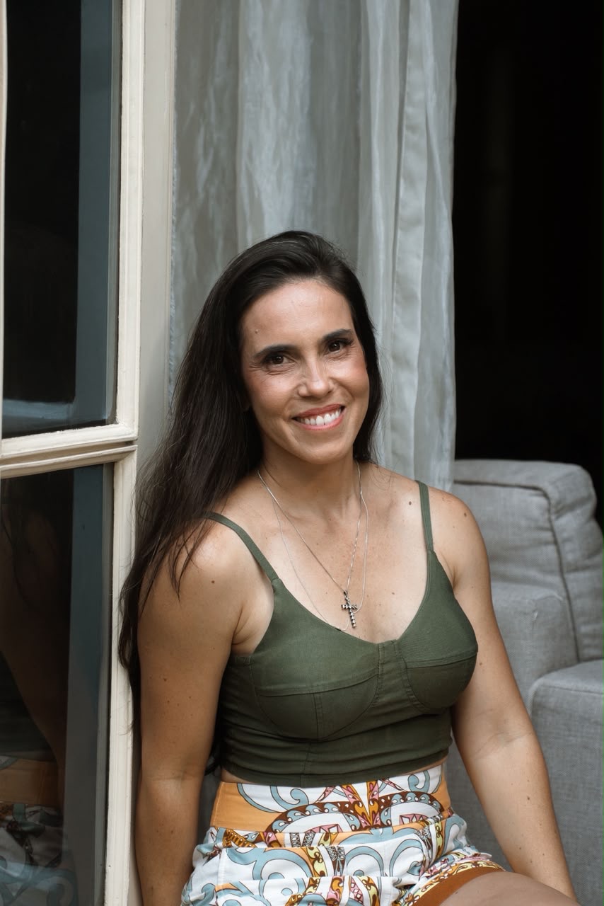 Érica Duque sentada junto à janela, sorrindo